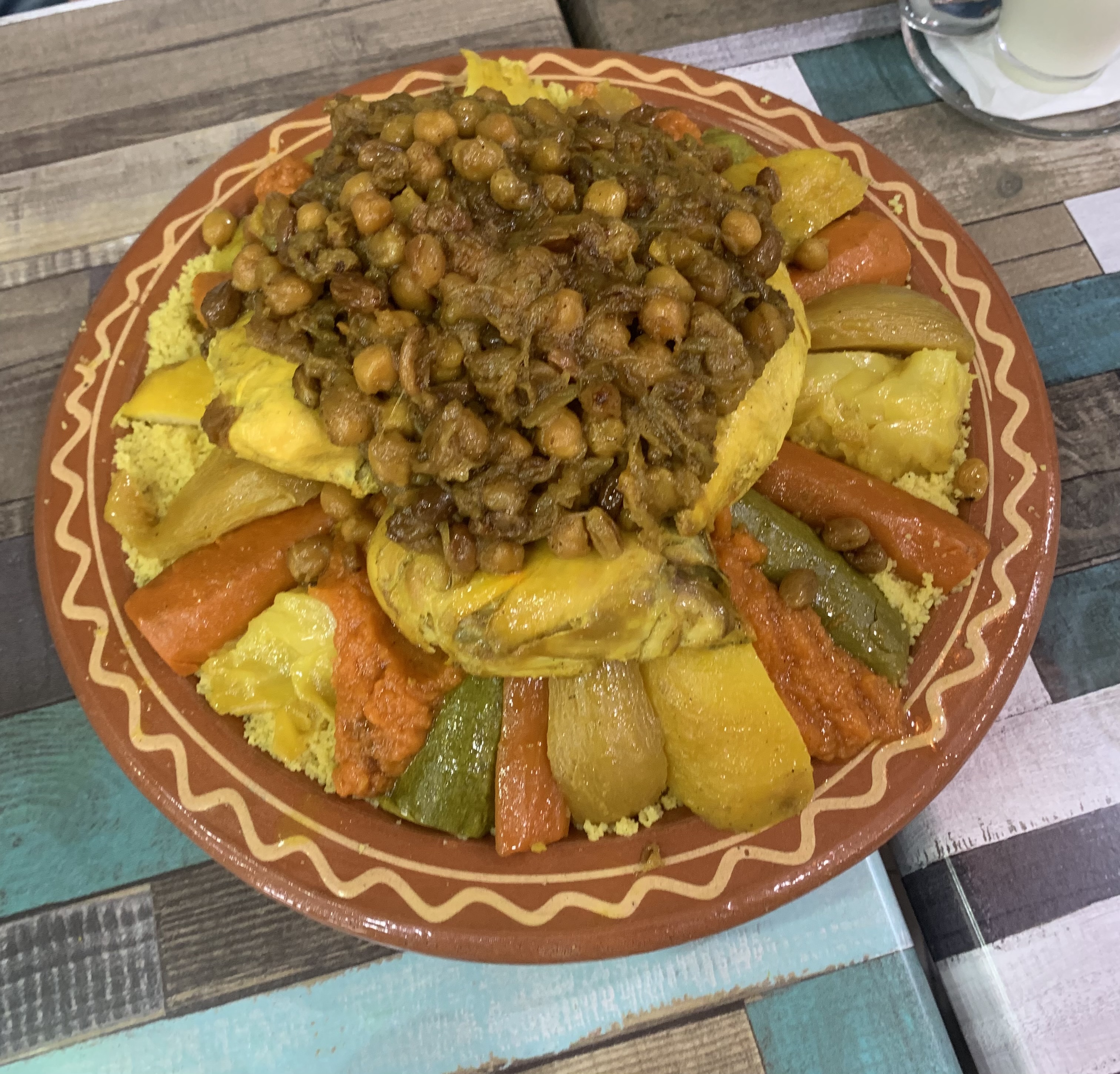 Real photograph of a large Moroccan couscous platter in a local Tétouan restaurant, with grain, vegetables, chickpeas, chicken and meat