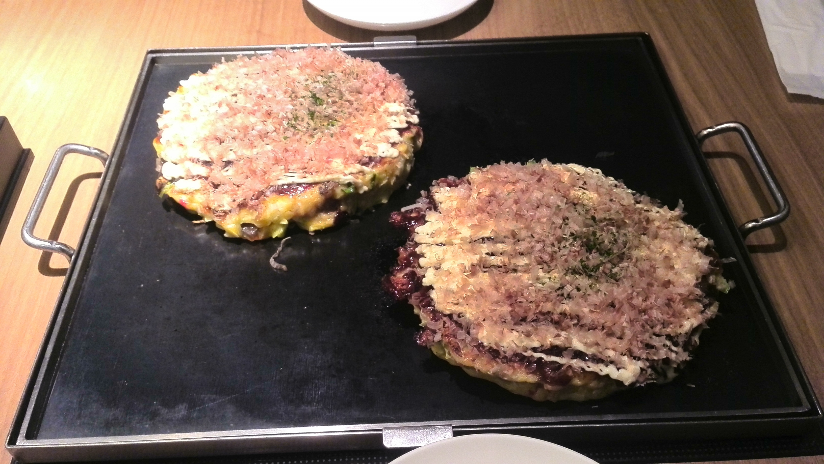 Real photograph of Osaka-style okonomiyaki topped with sauce, mayonnaise and aonori on a plate in Osaka