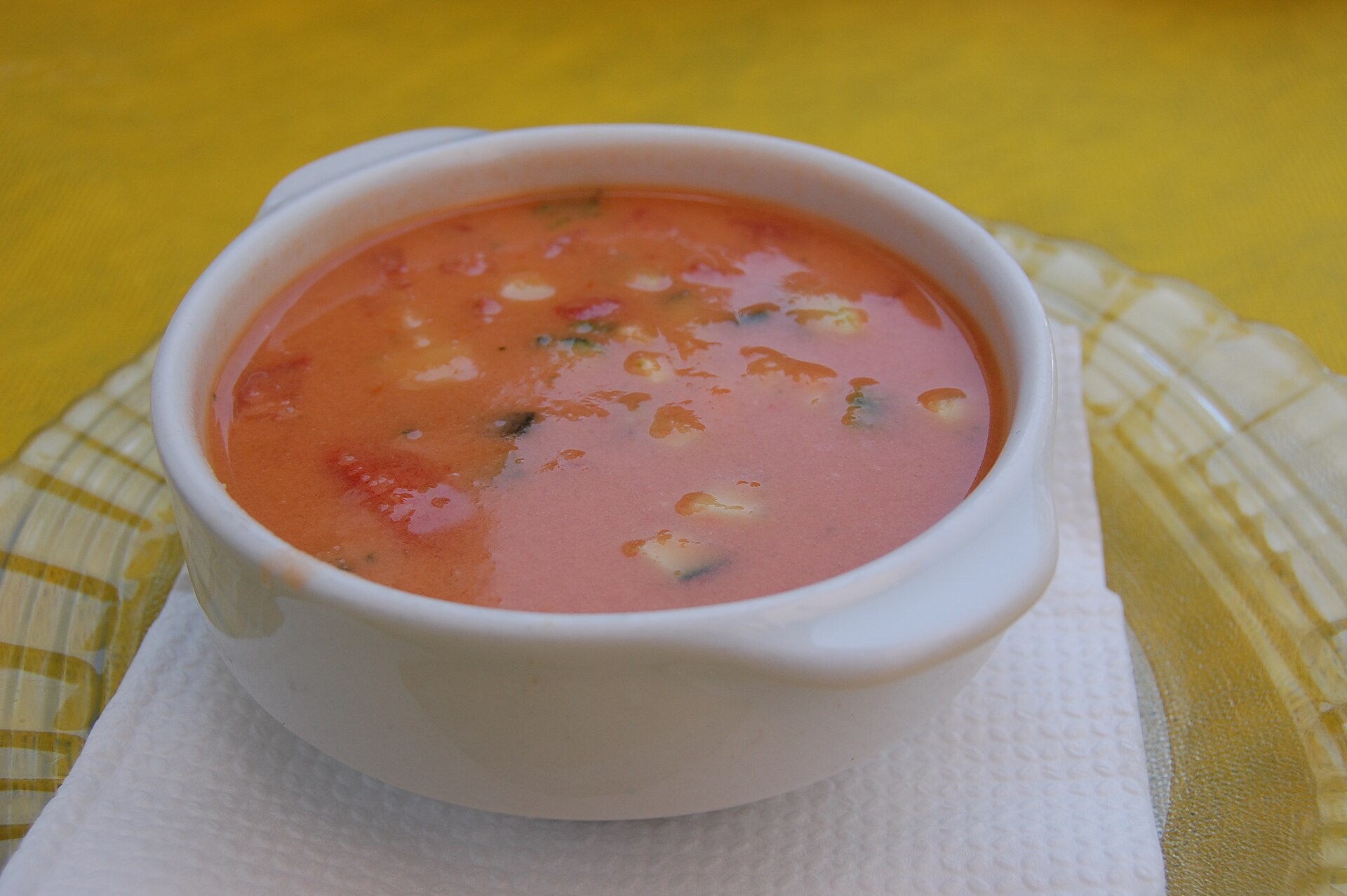 Real photograph of a bowl of red gazpacho served in Mijas, Andalusia, with finely diced vegetables on the side
